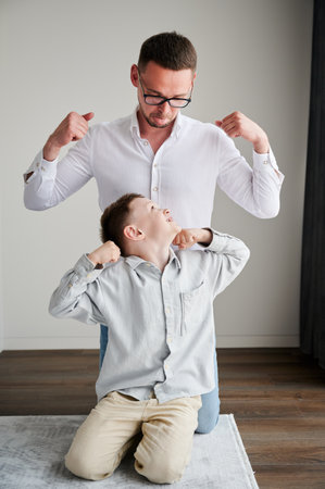 Young father playing with his curious son. Funny kid showing muscles to his dad. Family enjoying activity games at home.の写真素材