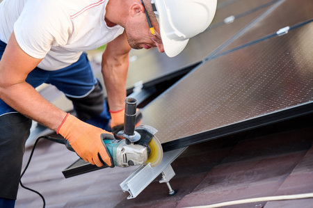 Worker installing or maintaining photovoltaic solar panel system on roof of house. Close up technician using grinder on metal part of the panels mounting structure. Concept renewable energy.の写真素材