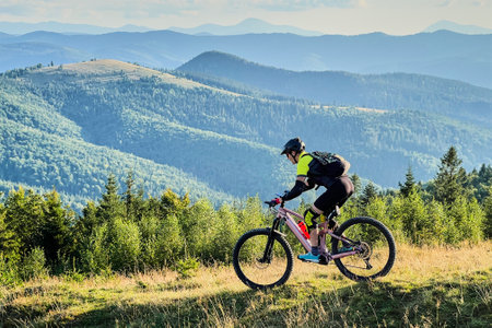 Cyclist man riding electric mountain bike outdoors. Male tourist biking along grassy trail in the mountains, wearing helmet and backpack. Concept of sport, active leisure and nature.の写真素材