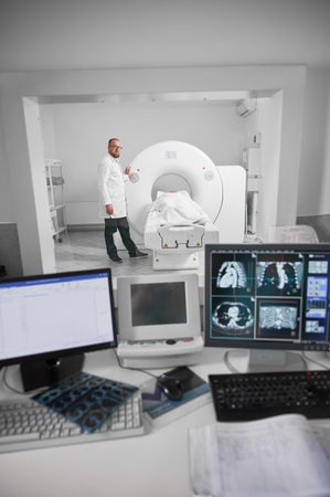Medical computed tomography or MRI scanner. Doctor making MRI, patient lying on couch. Male specialist wearing white robe and glasses, looking at camera, smiling. Concept of modern diagnostics.の写真素材