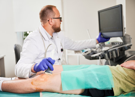 Doctor making ultrasound diagnostics, patient lying on couch. Focus on hand. Male specialist wearing uniform and glasses, looking at screen. Concept of medicine and healthcare.の写真素材