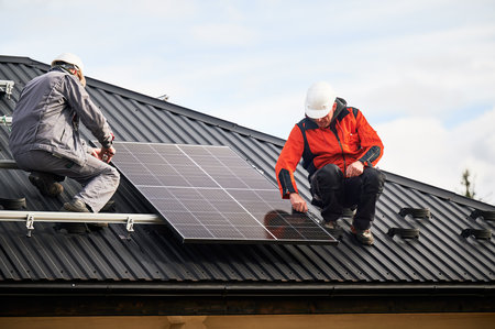 Mounters installing photovoltaic solar panels on roof of house. Men engineers in helmets building solar module system with help of hex key. Concept of alternative, renewable energy.の写真素材