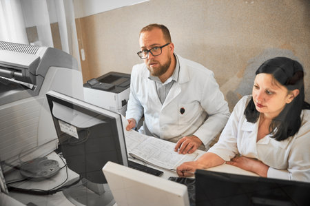 Two doctors working at computers. Specialists wearing white robes, making MRI, consulting, examining results. Concept of modern diagnostics.の写真素材