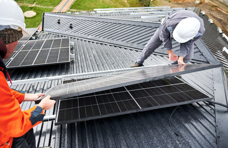 Workers building solar panel system on roof of house. Men technicians in helmets carrying photovoltaic solar module outdoors. Concept of alternative and renewable energy.の写真素材