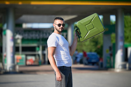 Confident man with canister finally found petrol station. Portrait of young male with empty canister in hand on background of gas station.の写真素材