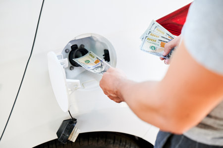 Pouring money into car tank. Cropped view of man must to spend a lot of money on gasoline. Fuel crisis concept.の写真素材