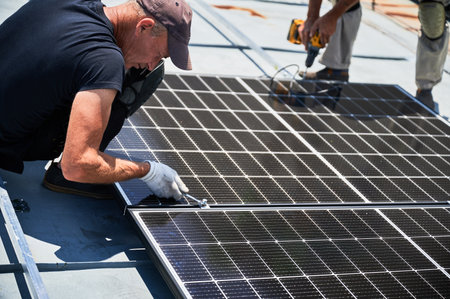Worker building photovoltaic solar panel system on rooftop of house. Close up of man engineer in gloves installing solar module with help of wrench outdoors. Renewable energy generation concept.の写真素材