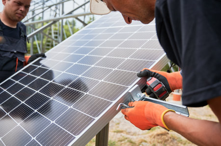 Workers installing solar panel on metal beams. Renewable and ecological energy. Idea of environment safe. Modern technology and innovation. Cropped image of european men wearing workwear and helmetsの写真素材