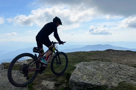Cyclist man riding electric mountain bike outdoors. Silhouette male tourist biking along grassy trail in the mountains, wearing helmet. Concept of sport, active leisure and nature.の写真素材