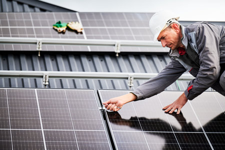 Man technician mounting photovoltaic solar panels on roof of house. Engineer in helmet installing solar module system with help of hex key. Concept of alternative, renewable energy.の写真素材