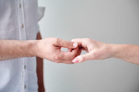 Close up of two hands engaging in delicate touch. Mans and womans hands on white neutral background. Husband holding hand of his lovely wife. Concept of love, intimacy, support, and trust.の写真素材