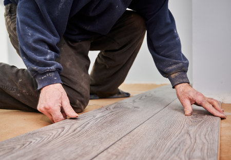 Close up of man construction worker installing laminate timber flooring in apartment under renovation. Male hands placing laminate planks on the floor at home. Flooring renovation concept.の写真素材