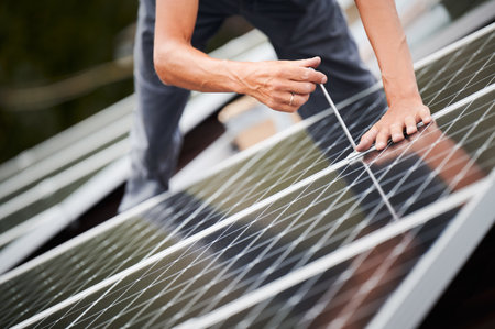 Man worker mounting photovoltaic solar moduls on roof of house. Close up of electrician installing solar panel system outdoors, tightening with hex key. Concept of alternative and renewable energy.の写真素材
