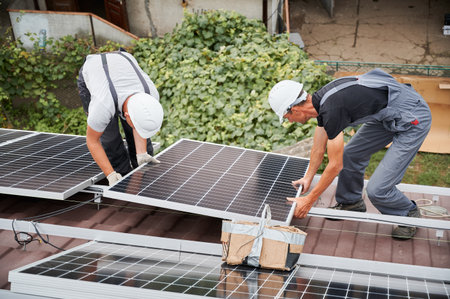 Men technicians installing photovoltaic solar moduls on roof of house. Engineers in helmets building solar panel system outdoors. Concept of alternative and renewable energy.の写真素材
