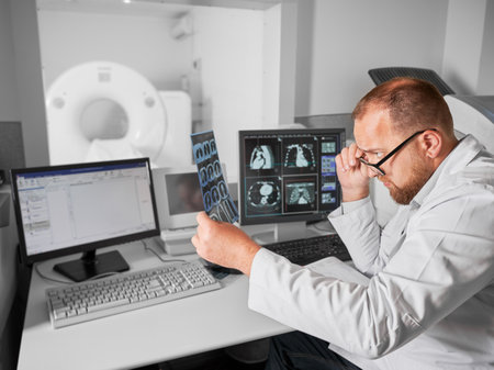 Medical computed tomography or MRI scanner. Side view of male doctor examining MRI results. Specialist wearing glasses and white robe, looking at x-ray, studying. Concept of medicine and healthcare.の写真素材