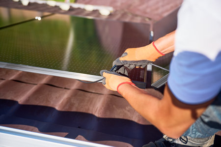 Worker installing solar panel system on roof of house. Close up electrician connecting modules together for generating electricity through photovoltaic effect. Concept of alternative, renewable energyの写真素材