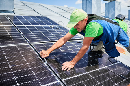 Worker building photovoltaic solar panel system on rooftop of house. Close up of man engineer installing solar module with help of wrench outdoors. Alternative and renewable energy generation concept.の写真素材