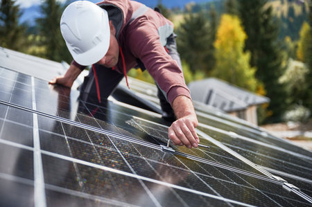 Man technician mounting photovoltaic solar panels on roof of house. Engineer in helmet installing solar module system with help of hex key. Concept of alternative, renewable energy.の写真素材