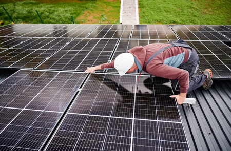 Technician mounting photovoltaic solar panels on roof of house. Man engineer in helmet installing solar modules system outdoors. Concept of alternative and renewable energy.の写真素材