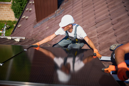 Worker building solar panel system on rooftop of house. Man engineer in helmet installing photovoltaic solar module outdoors. Alternative, green and renewable energy generation concept.の写真素材