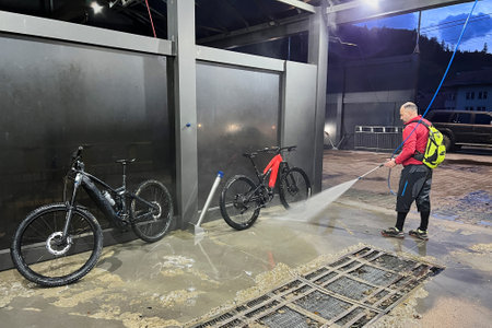 Cyclist using high-pressure water spray to clean two electric mountain bikes on outdoor washing station.の写真素材