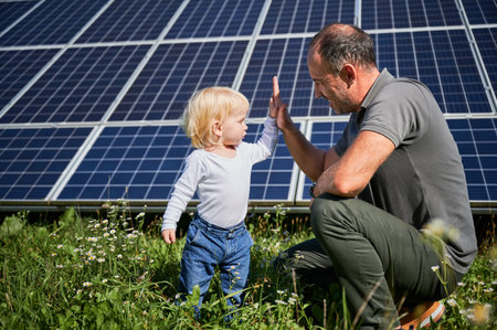 Young father and his little son giving each other high-five on background of solar panels. Young father glad spending time with his child. Happy family of two on background of solar panels.の写真素材