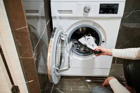 Dirty sport shoes need to be washed. Cropped photo of woman putting sneaker in washing machine.の写真素材
