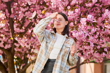 Woman allergic suffering from seasonal allergy at spring. Beautiful woman with clothespin clipped to his nose - symbolic gesture of his inability to breathe due to nasal congestion near blooming tree.の写真素材