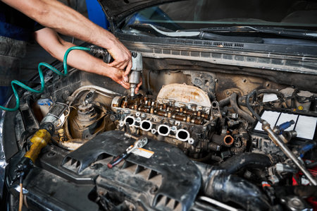Close up of repairman, mechanic repairing, fixing car engine. Man worker working in garage, workshop, auto servicing center, twisting off engine. Concept of servicing autos.の写真素材