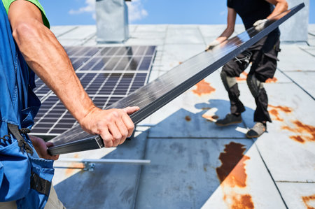 Workers building solar panel system on metal rooftop of house. Two men installers carrying photovoltaic solar module outdoors. Alternative, green and renewable energy generation concept.の写真素材