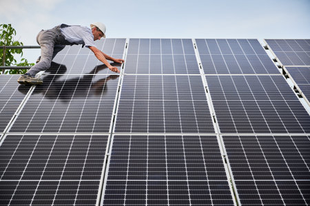 Male worker building photovoltaic solar panel system outdoors. Man electrician placing solar module on metal rails, wearing construction helmet. Renewable and ecological energy.の写真素材