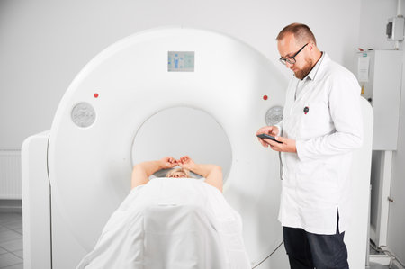 Medical computed tomography or MRI scanner. Doctor holding mobile phone and examining results of MRI. Woman patient lying on couchette. Concept of medicine, healthcare and modern diagnostics.の写真素材