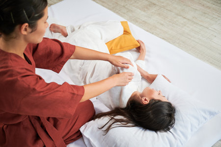 Masseuse making thai yoga massage. Woman therapist doing traditional massage treatment for female patient. Client lying on mat, meditating, enjoying hand massage in calm atmosphere. Cropped view.の写真素材