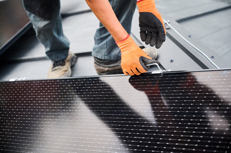 Worker building photovoltaic solar panel system on rooftop of house. Man engineer in gloves installing solar module with help of hex key outdoors. Alternative and renewable energy generation concept.の写真素材