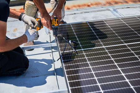 Workers building photovoltaic solar panel system on metal rooftop of house. Close up man technician...