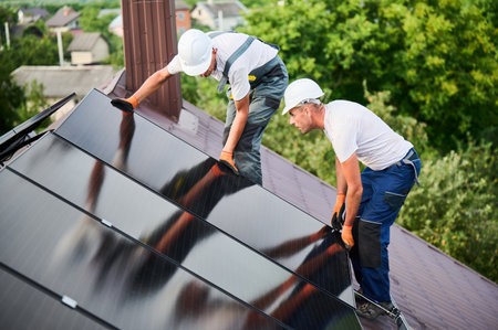 Workers building solar panel system on rooftop of house. Two men installers in helmets installing photovoltaic solar module outdoors. Alternative, green and renewable energy generation concept.の写真素材