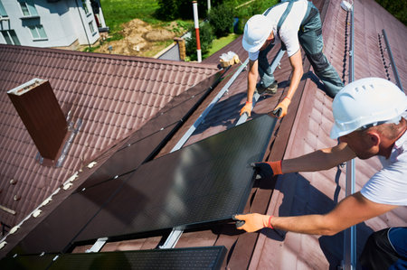 Workers building solar panel system on rooftop of house. Two men installers in helmets installing...
