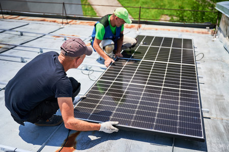 Workers building solar panel system on metal rooftop of house. Two men installers installing...
