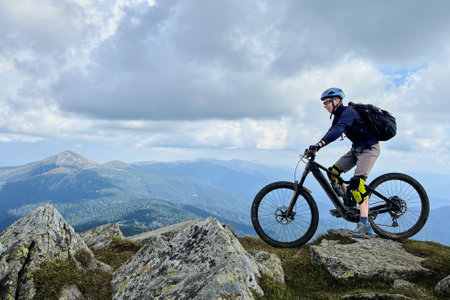 Cyclist man riding electric mountain bike outdoors. Male tourist biking along grassy trail in the mountains, wearing helmet and backpack. Concept of sport, active leisure and nature.の写真素材