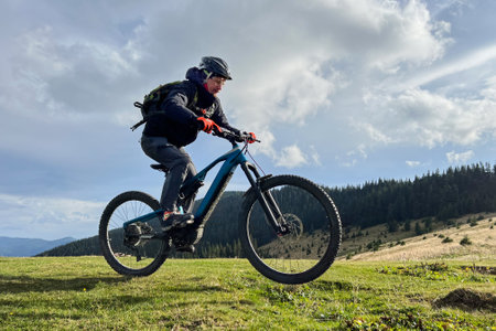 Cyclist man riding electric mountain bike outdoors. Male tourist biking along grassy trail in the mountains, wearing helmet and backpack. Concept of sport, active leisure and nature.の写真素材