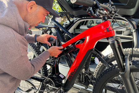 Close up of man adjusting electric mountain bike mounted on vehicle bike rack. Persons attention to detail suggests careful preparation or check before ride.の写真素材