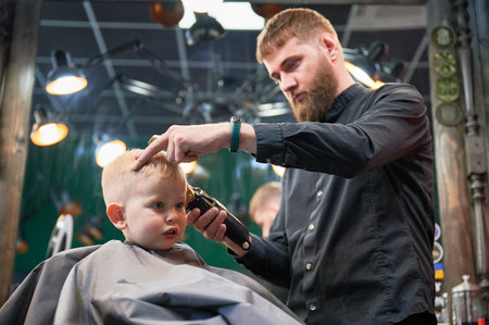 Barber using comb and shaver to cut hair. Professional hairdresser shaving little kids nape.の写真素材