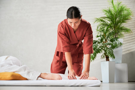 Masseuse making thai yoga massage. Woman therapist doing traditional massage treatment for female patient indoors. Client lying on mat, meditating, enjoying hand massage in calm atmosphere.の写真素材