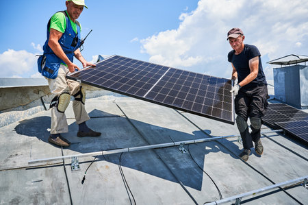 Workers building solar panel system on metal rooftop of house. Two men installers carrying photovoltaic solar module outdoors. Alternative, green and renewable energy generation concept.の写真素材