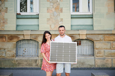 Cute couple holding portable solar panel. Young man and his wife showing their green lifestyle. Concept of integration of sustainable renewable energy sources within city environments.の写真素材