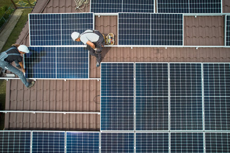 Men technicians mounting photovoltaic solar moduls on roof of house. Workers in helmets installing solar panel system outdoors. Concept of alternative and renewable energy. Aerial view.の写真素材