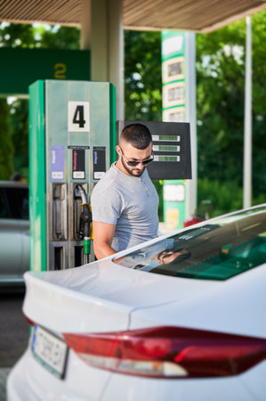 Skilled driver refueling gas tank in his automobile for long road. Man standing next to car on background gas column.の写真素材