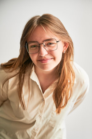 Portrait of beautiful girl smiling to camera. Cute girl in cream shirt and square glasses posing on white background.の写真素材