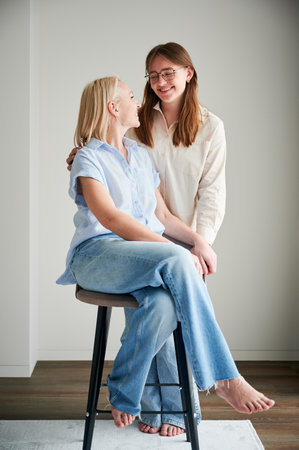 Cute family moment of mom and daughter hugging. Portrait of teenage girl showing her love to mother. Two female in casual clothes smiling and hugging at home.の写真素材