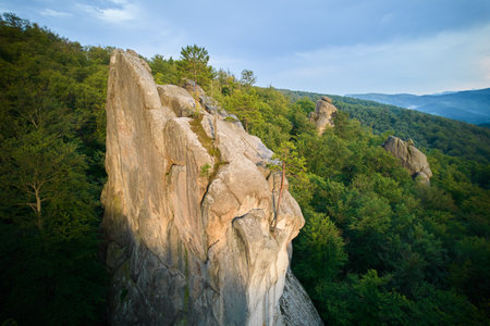 Aerial view of rock formation bathed in warm sunlight among lush green forest and rolling hills. Dovbush Rocks, Carpathian mountains, Ukraine.の写真素材